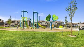 Un parque infantil con toboganes y estructuras para escalar, rodeado de césped y edificios residenciales.