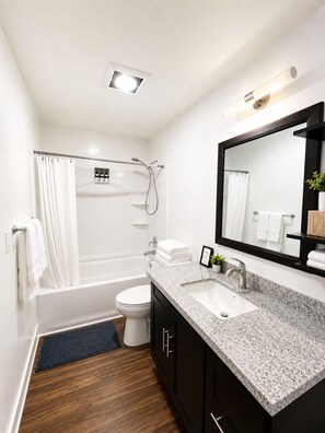 A modern bathroom with a bathtub, toilet, sink, and a large mirror. - 2BR/2BA in Queen Anne | Near Downtown Seattle Center I AC and driveway parking (Seattle)