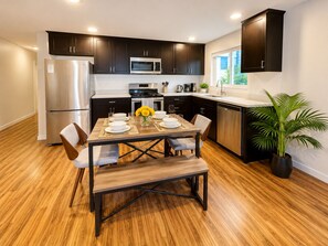 A modern kitchen with dark cabinets, stainless appliances, and a wooden dining table set for four.