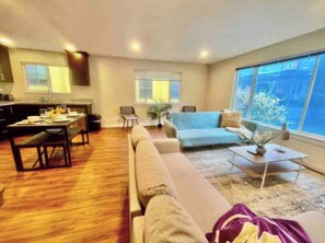 A modern living room with a sofa, a dining table, and a coffee table. There is a large window providing a view of the outdoors. - 2BR/2BA in Queen Anne | Near Downtown Seattle Center I AC and driveway parking (Seattle)