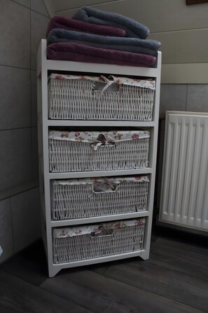 Ein weißes Korbmöbelregal mit mehreren Fächern, einige gefüllt mit Stoffen mit Blumenmuster.