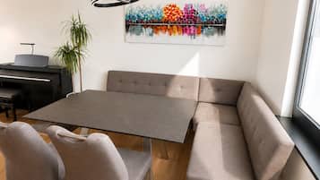Uma zona de refeições moderna com uma mesa cinzenta, duas cadeiras cinzentas, um sofá e um piano.