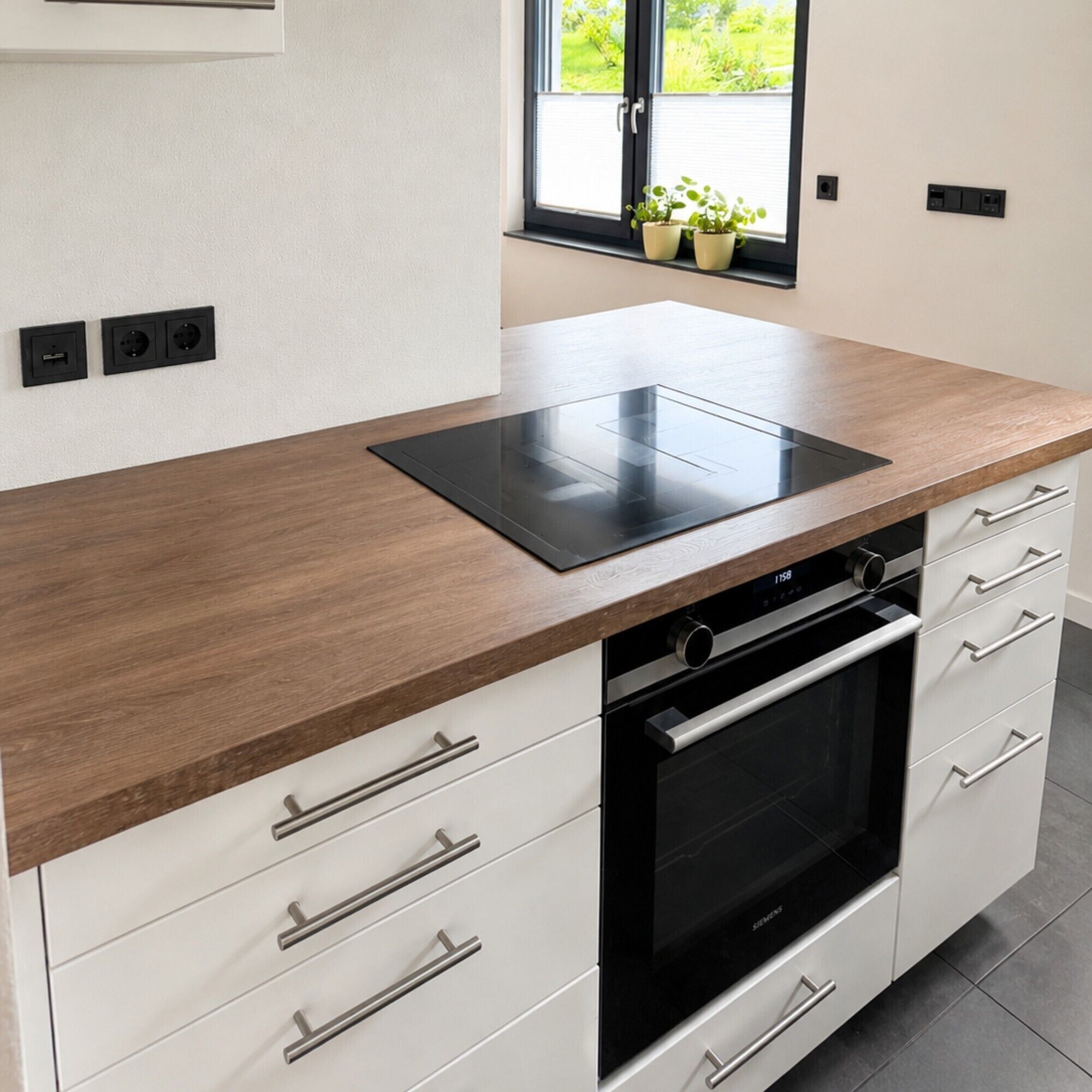 A modern kitchen with a built-in oven, a black induction cooktop, and white cabinetry.