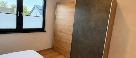 A bedroom with a large bed, a sliding door, and a window with a view of a house.