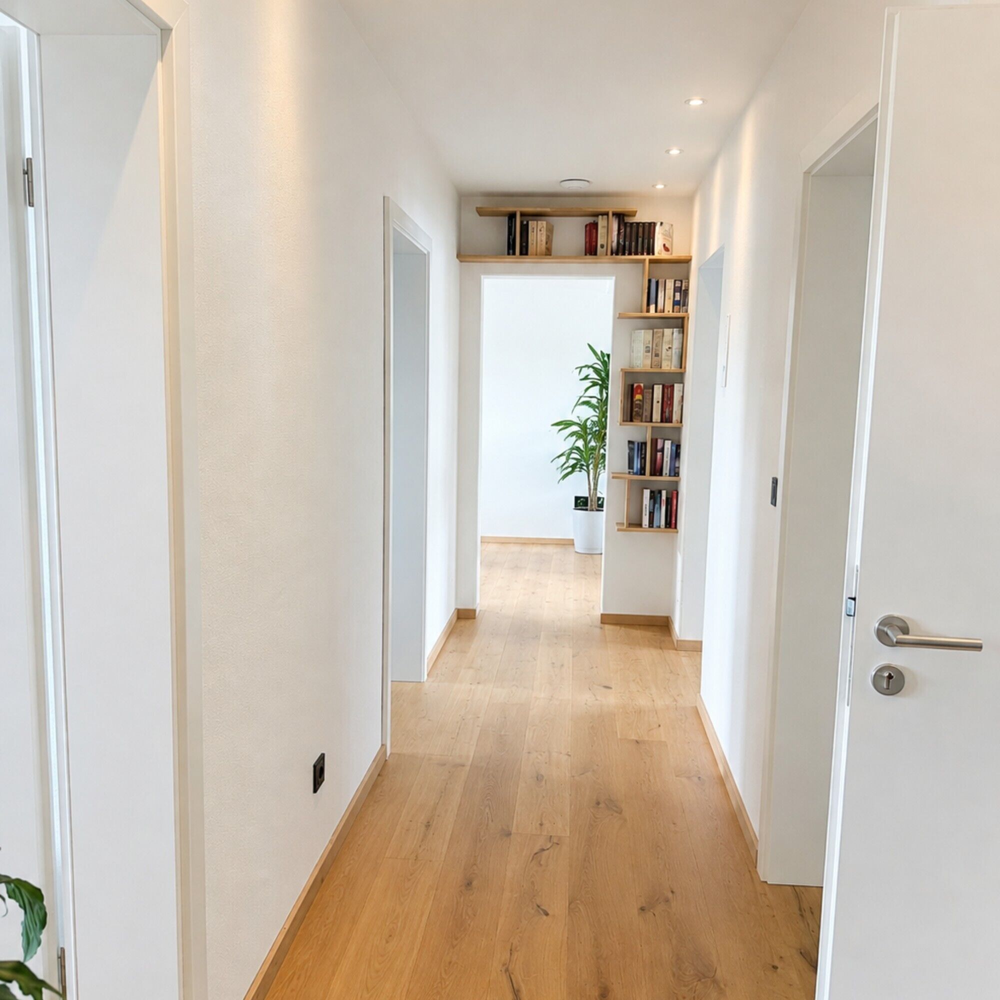 Ein Flur mit Holzboden, weißen Wänden und einem Bücherregal voller Bücher.