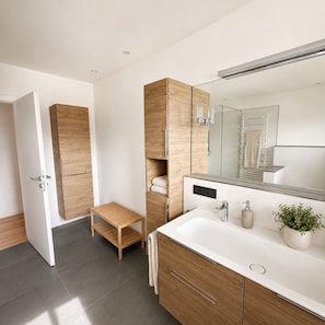 A modern bathroom with a large mirror, a white sink, wooden cabinets, and a small wooden stool. - Apartment 'Haus Biggeglück' with Private Roof Terrace & Walk to Lake Biggesee (Olpe)