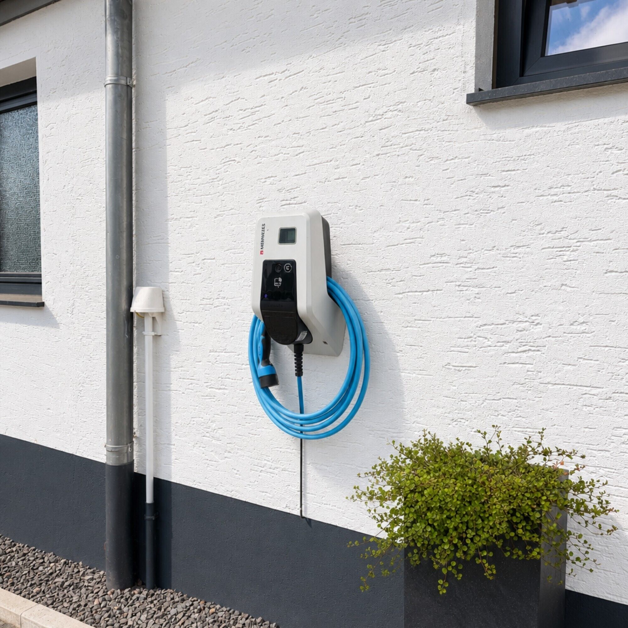 Estação de carregamento para veículo elétrico fixada em uma parede branca, com um cabo azul conectado.