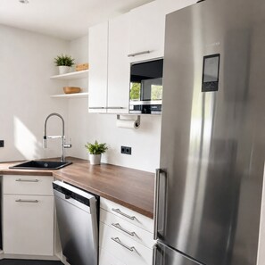 A modern kitchen with stainless steel appliances, white cabinetry, and a wooden countertop. - Apartment 'Haus Biggeglück' with Private Roof Terrace & Walk to Lake Biggesee (Olpe)