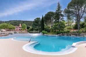 Une piscine avec un bassin aux eaux d’un bleu limpide, entourée d’un espace paysager agrémenté d’arbres et avec un bâtiment en arrière-plan.