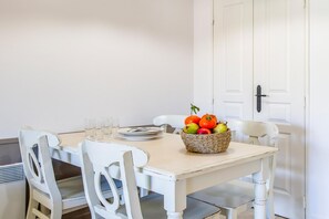 Une table à manger avec des chaises, un panier de fruits et, au fond, une porte blanche.