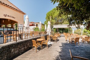 Un espace café en plein air avec des tables et des chaises en bois, des parasols blancs et un mur en pierre.