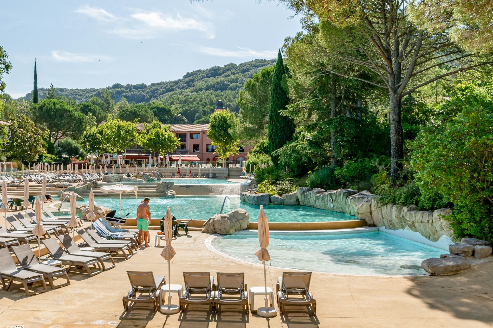 A pool area with lounge chairs, umbrellas, and a view of a hill.