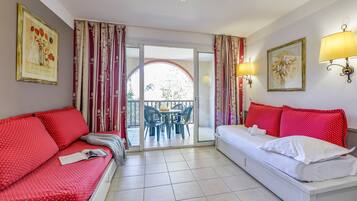 Ein Hotelzimmer mit Bett, einer Couch, einem Esstisch mit Stühlen und einem Balkon mit Vorhängen.