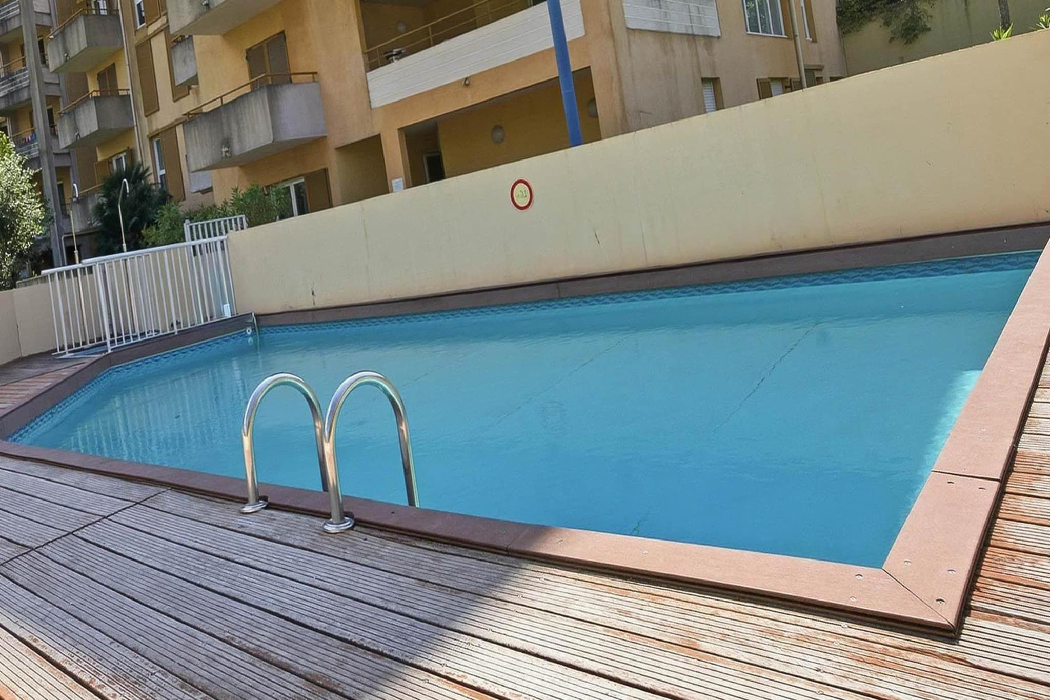 A rectangular swimming pool with two metal ladders on one side, surrounded by a wooden deck.