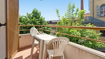A balcony with a table and chairs, a railing, and a view of greenery and buildings.