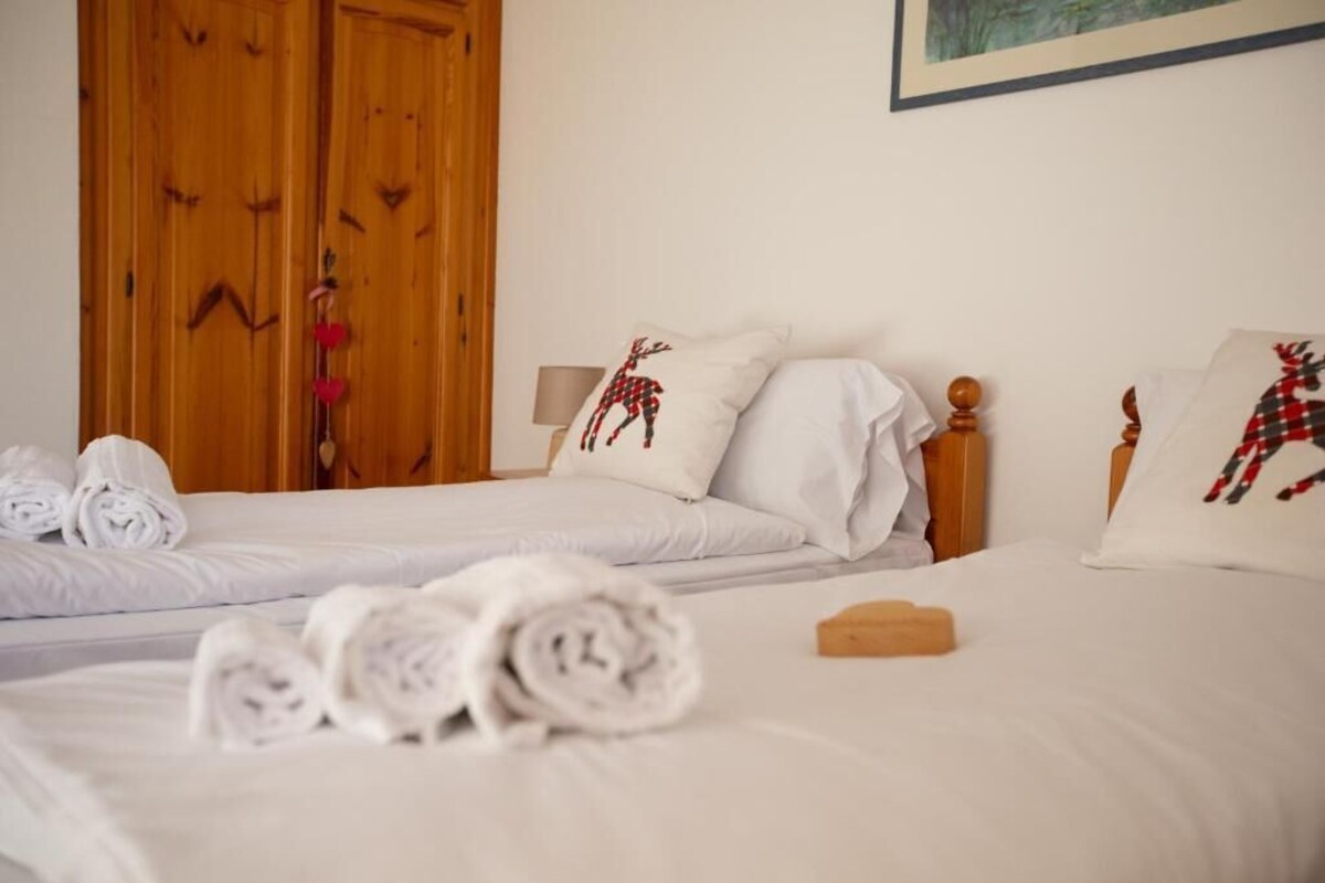 A hotel room with two beds, white linens, and decorative pillows with reindeer designs.