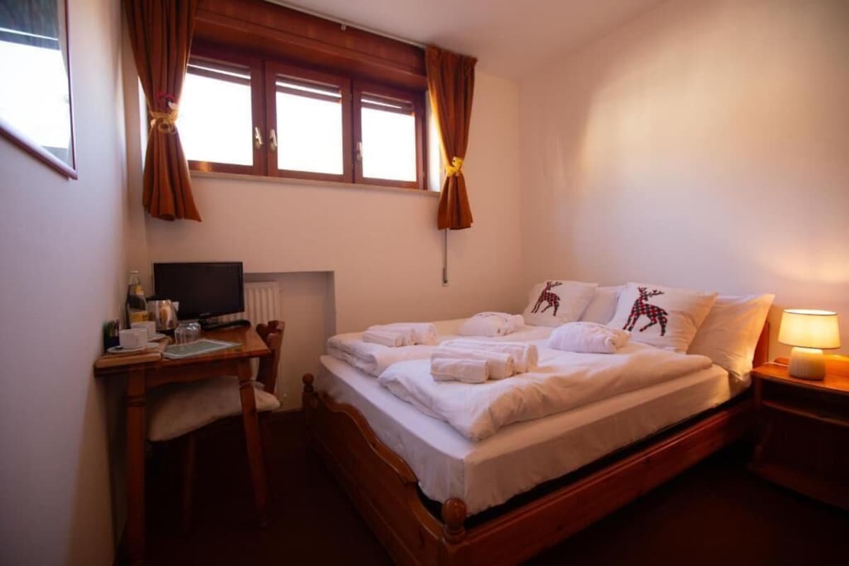 A hotel room with a bed, a desk with a computer, a chair, and a nightstand with a lamp.