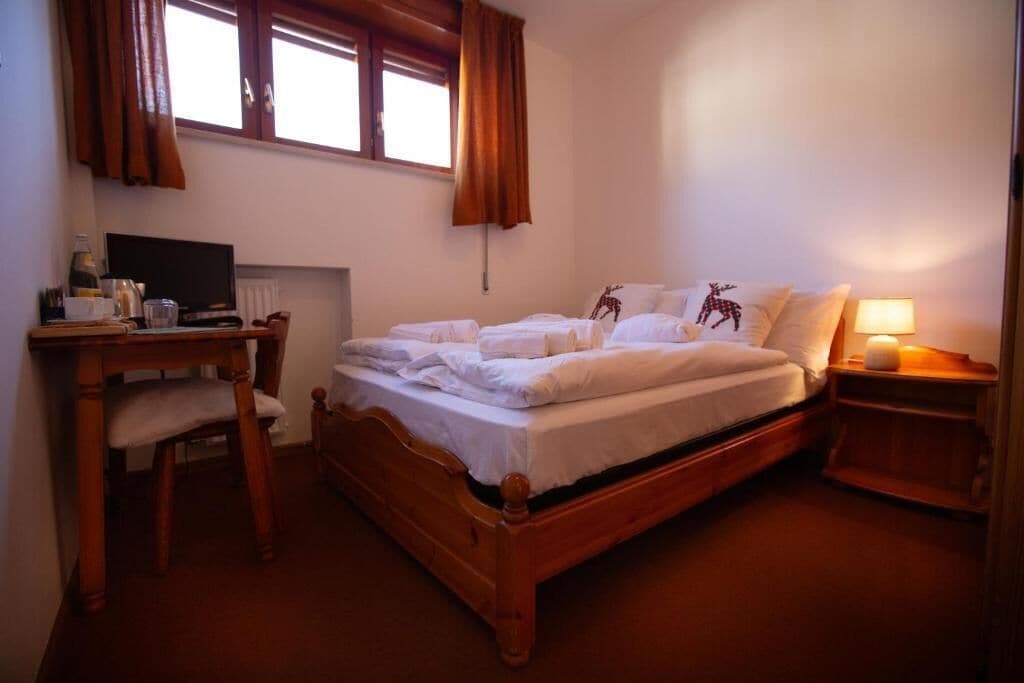 A bedroom with a wooden bed, a desk with a computer, and a window with curtains.