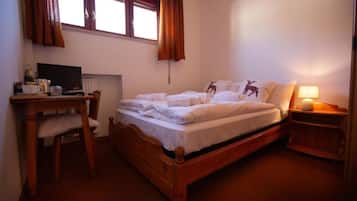 A bedroom with a wooden bed, a desk with a computer, and a window with curtains.