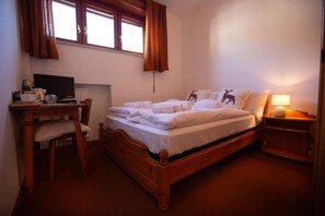 Un dormitorio con una cama de madera, un escritorio con computadora y una ventana con cortinas.