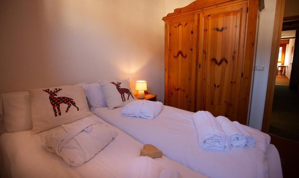 Habitación de hotel con una cama, dos almohadas con diseños de renos, un armario de madera y una mesita de noche con una lámpara.