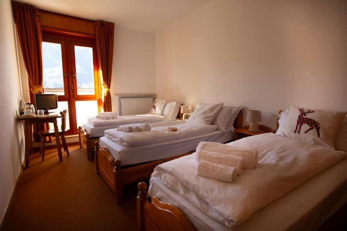 A hotel room with two beds, a desk, and a window with curtains.
