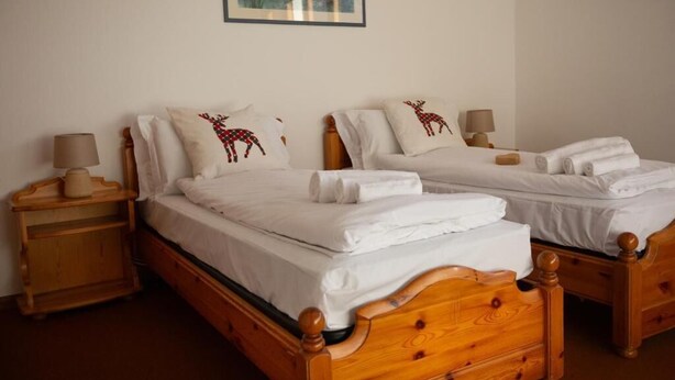 A double bed with a wooden headboard, white bedding, and decorative pillows with reindeer designs. - Bike & Bikers Hotel (Ampezzo)
