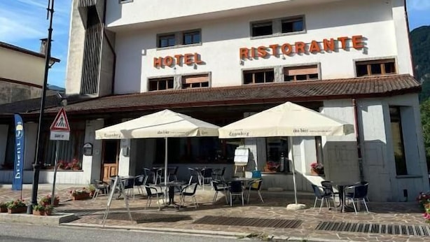 A hotel with a restaurant on the ground floor, outdoor seating with umbrellas, and a clear sky. - Bike & Bikers Hotel (Ampezzo)