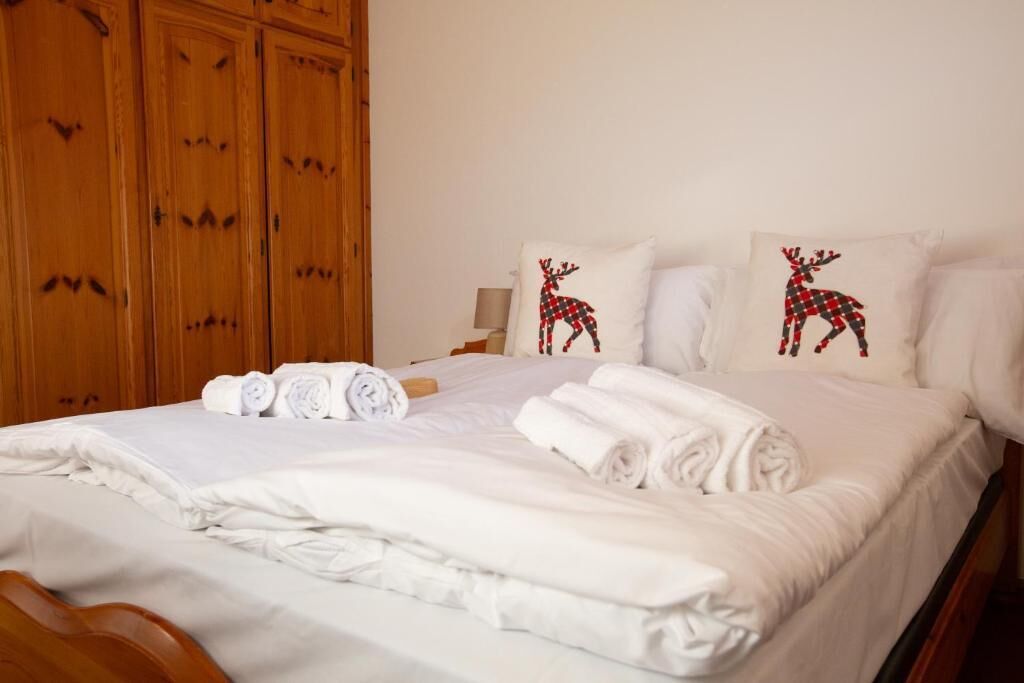 Un lit bien fait, avec du linge de lit blanc et des serviettes pliées, une armoire en bois et deux oreillers ornés d’un motif de renne.
