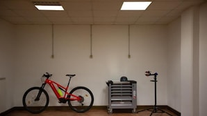 A room with a wooden floor, a red bicycle, a grey storage cart, and a tripod stand. - Bike & Bikers Hotel (Ampezzo)