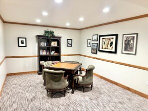 A conference room with a wooden table, four chairs, a bookshelf, and framed pictures on the walls. - 2073 | Designer King Villa | Full Kitchen | Pool (Midway)