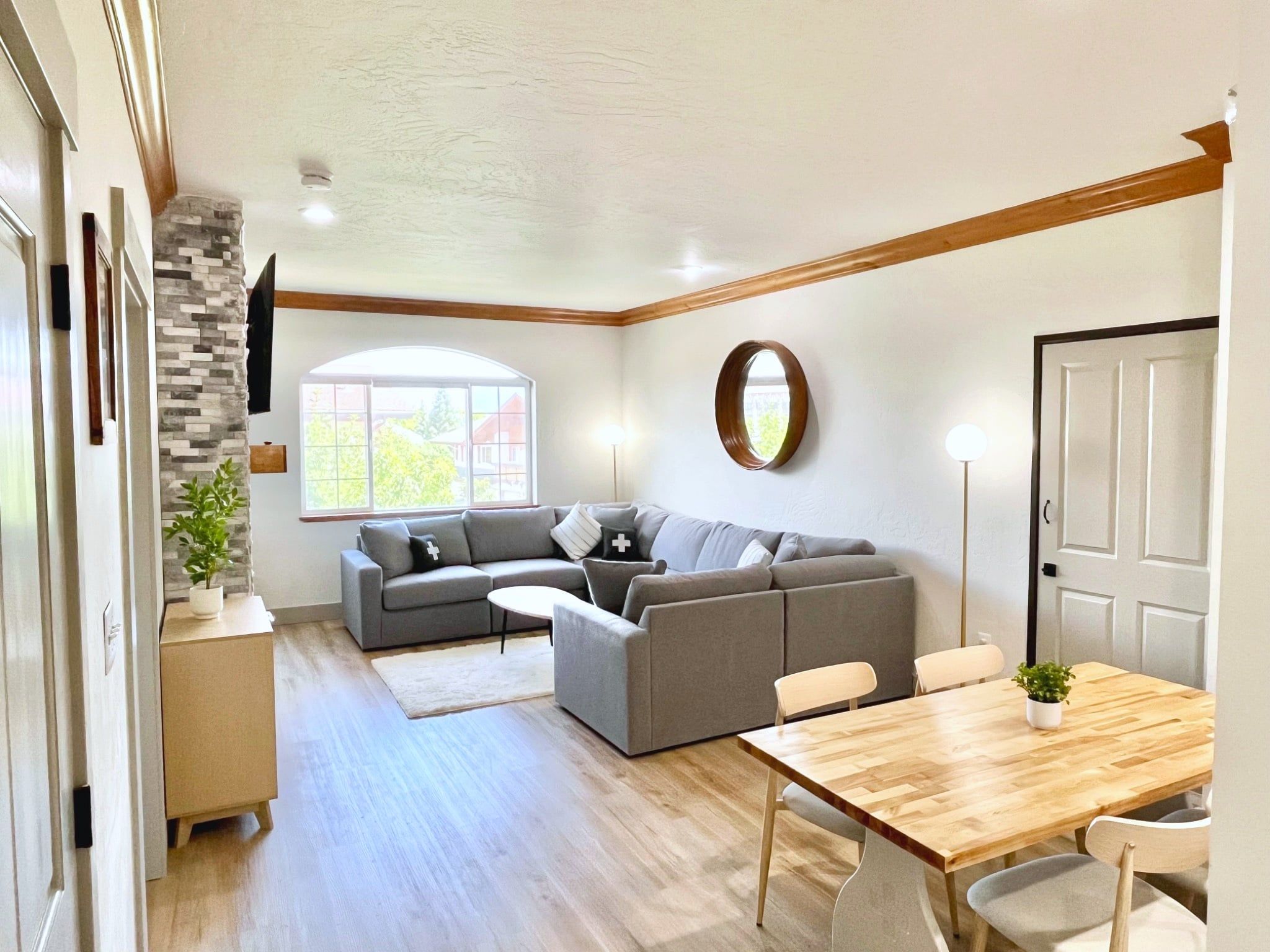 A modern living room with a sectional sofa, a dining table with chairs, and a large window providing natural light.