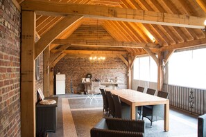 Een landelijke eethoek met een lange houten tafel, rieten stoelen en een achtergrond van een metselwerk muur.