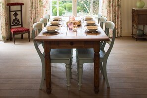 Mesa de comedor dispuesta para seis personas, con sillas, cortina floral y vista al exterior.