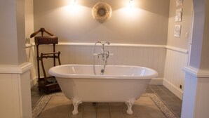 Ein Badezimmer mit einer freistehenden Badewanne, einem Holzstuhl und einer Wandleuchte.