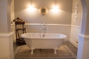 Een badkamer met een vrijstaand bad, een houten stoel en een wandlamp.