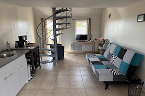 En kompakt bolig med tekøkken, sofa, TV og en spiraltrappe.