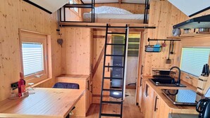Eine gemütliche Holzhütte mit Etagenbett, Küchenzeile und Esstisch.