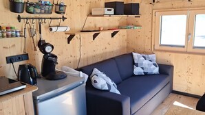 Ein kompakter Wohnraum mit Küchenzeile, einer Couch mit gemusterten Kissen und einem Fenster, das natürliches Licht hereinlässt.