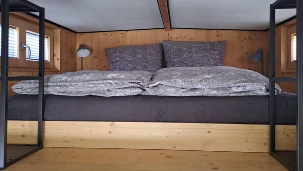Ein Stockbett mit Holz Kopfteil und einer grau gemusterten Bettdecke.