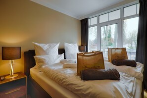Ett hotellrum med en säng, kuddar, en sänglampa, ett fönster med gardiner och en väska på sängen.