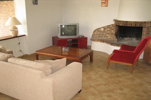 A living room with a sofa, a red chair, a coffee table, a television on a stand, and a fireplace. - Normandy Gite with Bay Views (Courtils)