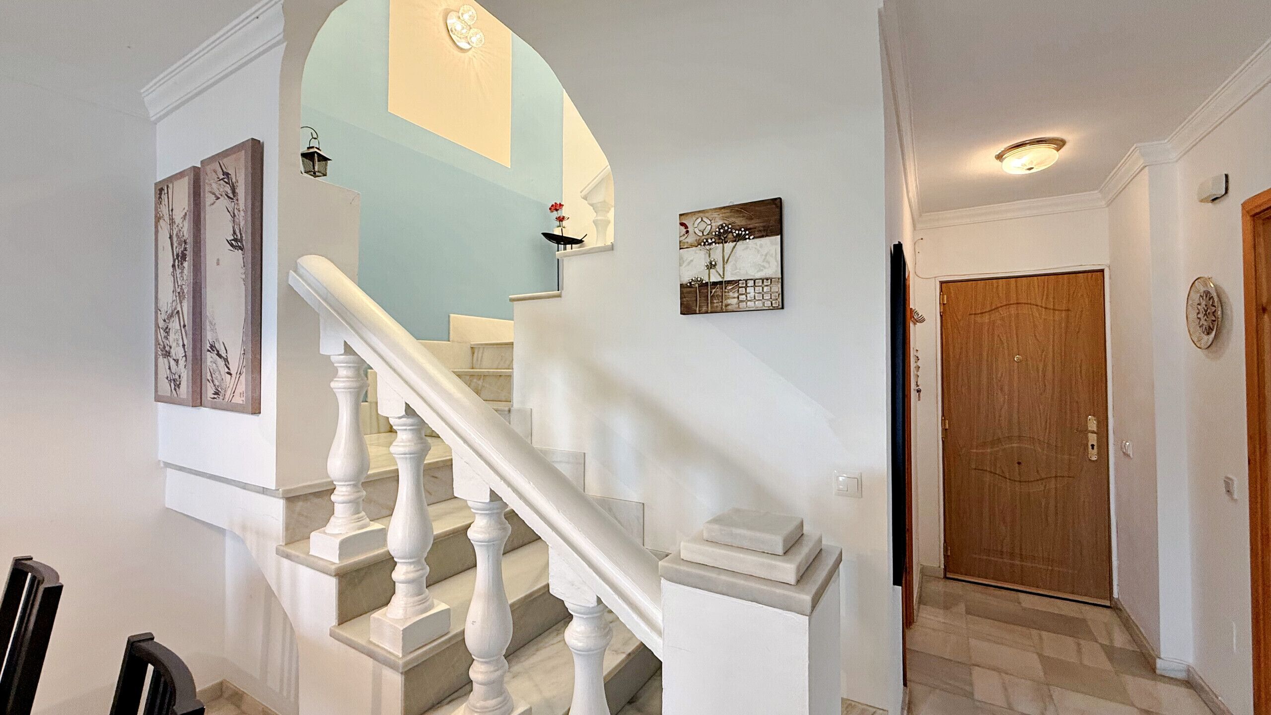 A staircase with white balusters leading to a landing with a light fixture and artwork.