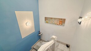 A bathroom with a blue wall, a white towel rack, a shelf with candles, and a wall-mounted light fixture. - AP433 VILLA LA NORIA (Nerja)