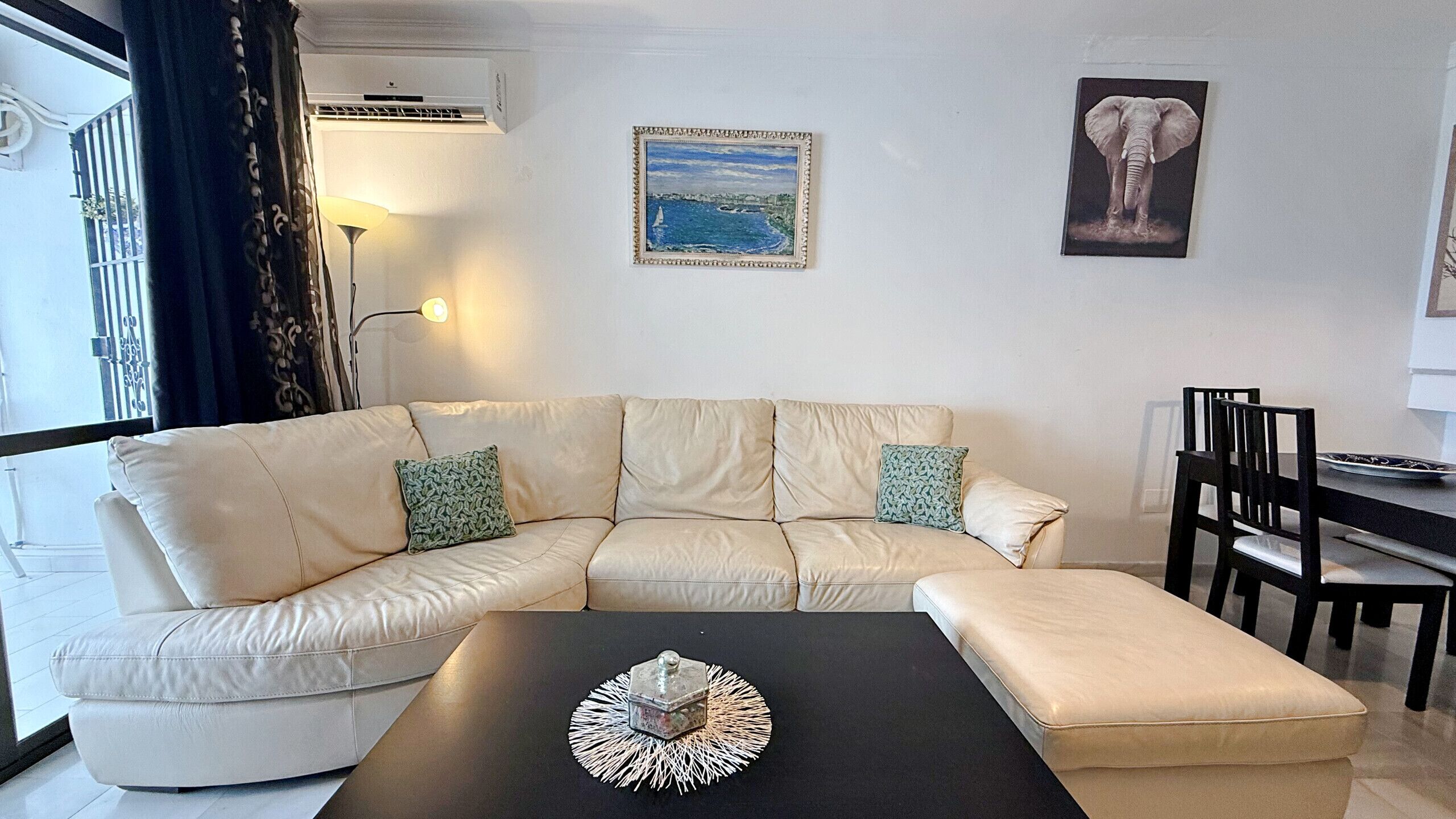 Una sala de estar con un sofá seccional color beige, una mesa de centro negra y dos cuadros enmarcados en la pared.