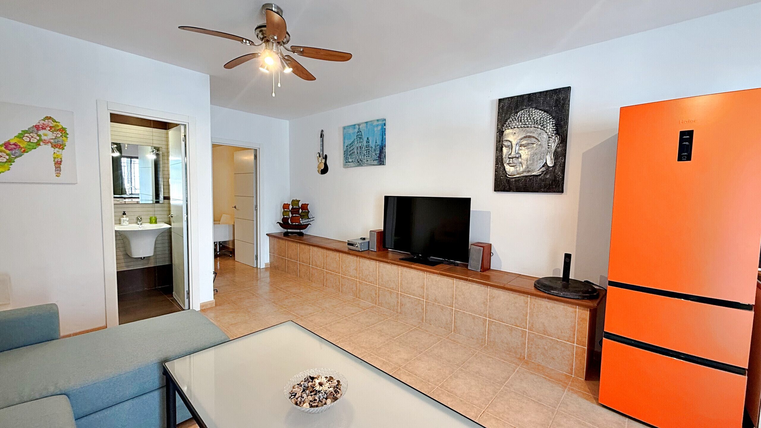 Una sala de estar moderna con un sofá, una mesa de centro, un televisor y un ventilador de techo.