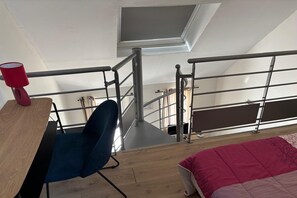 A room with a desk, chair, and a bed with a red blanket. There is a window with a view of the outside. - Charming Normandy Escape for Three (Courtils)