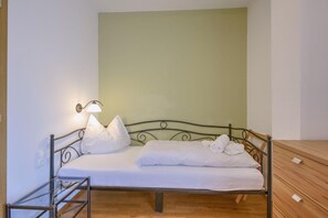 A single bed with a metal frame, white bedding, and a wall-mounted lamp. - Apartment in Wildschönau Vicky small apartment (Wildschönau)