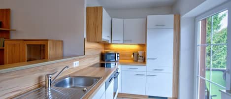 A modern kitchen with a stainless steel sink, wooden countertop, and white cabinets.