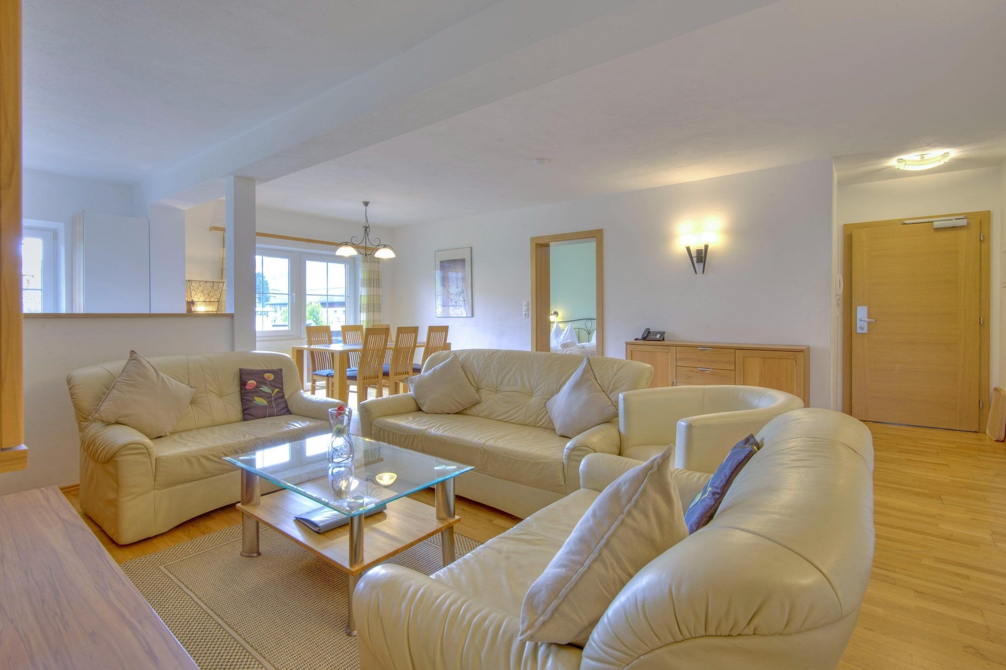 Ein geräumiges Wohnzimmer mit einer großen, winkelförmigen Couch, einem Glastisch und einem Essbereich mit Holzsesseln.